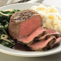 Center-of-the-plate filet mignon sliced four times, cooked medium rare. Mashed potatoes on right, cooked spinach on left