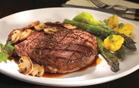 Plate of grilled steak covered with mushroom sauce, served with asparagus and yellow summer squash