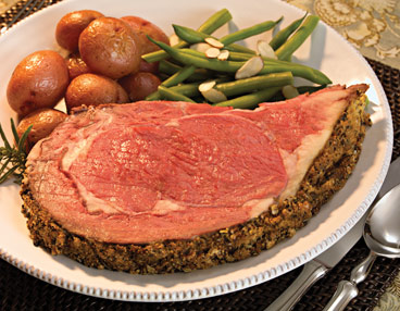 White plate filled with slice of rare prime rib. Roasted red potatoes and green beans almandine at top of plate