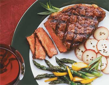 Plate of sliced New York steak, asparagus with sliced yellow bell peppers and sliced, seasoned radishes