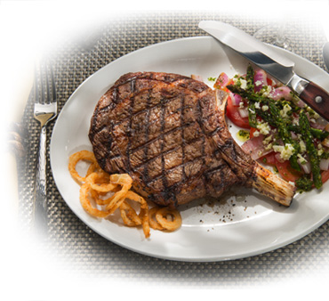 Plate of grilled bone-in ribeye with onion rings and vegetable medley