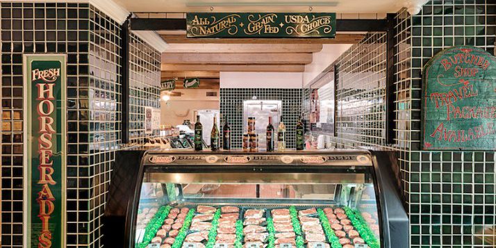 Stocked meat case at Harris Ranch Inn & Restaurant, Sign above: Harris Ranch Beef Company, All Natural, Grain Fed, USDA Choice. Green tiles on wall with white grout surround meat case. Sign on left says: Fresh Horseradish