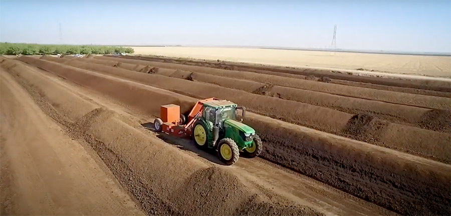 Tractor driving between rows of piled compost taken from Harris Feeding Company feedlot